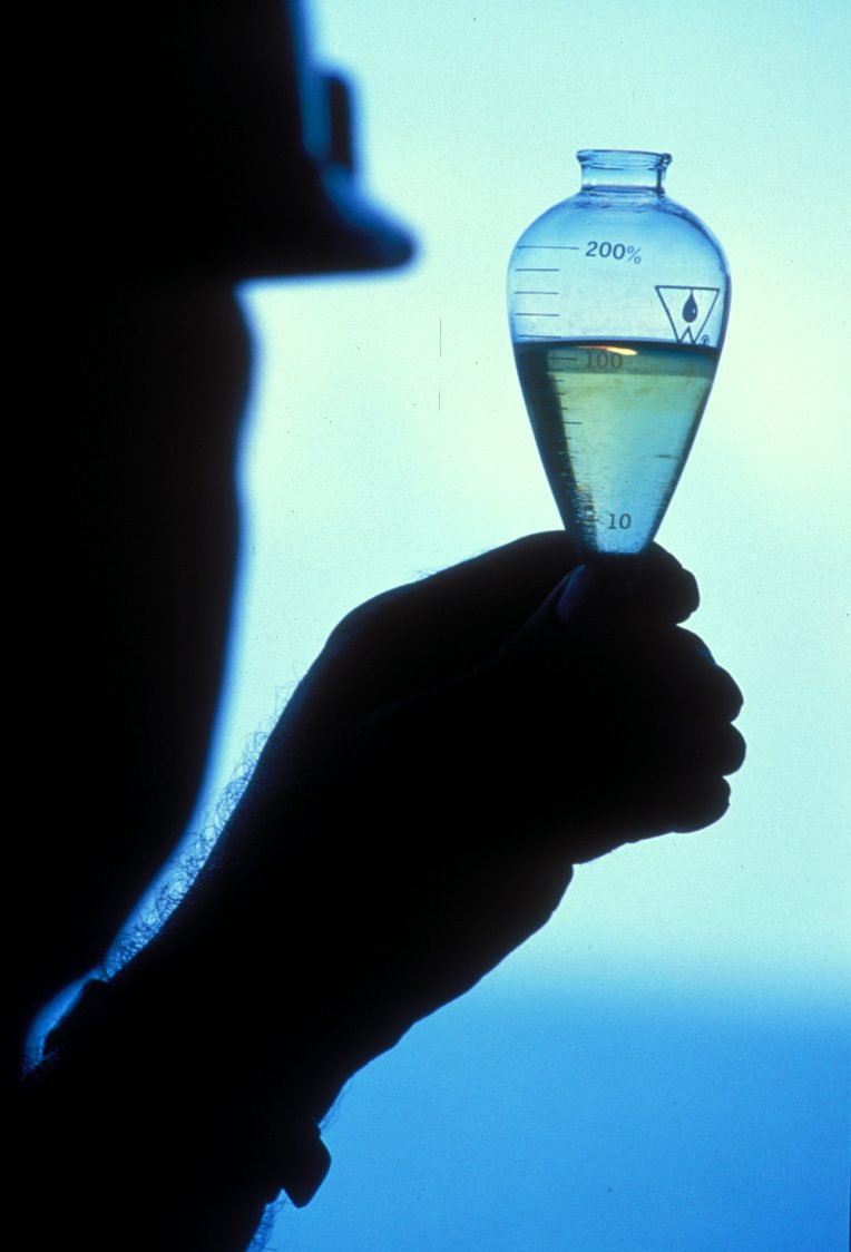 Silhouetted hand holding a glass sample flask against light